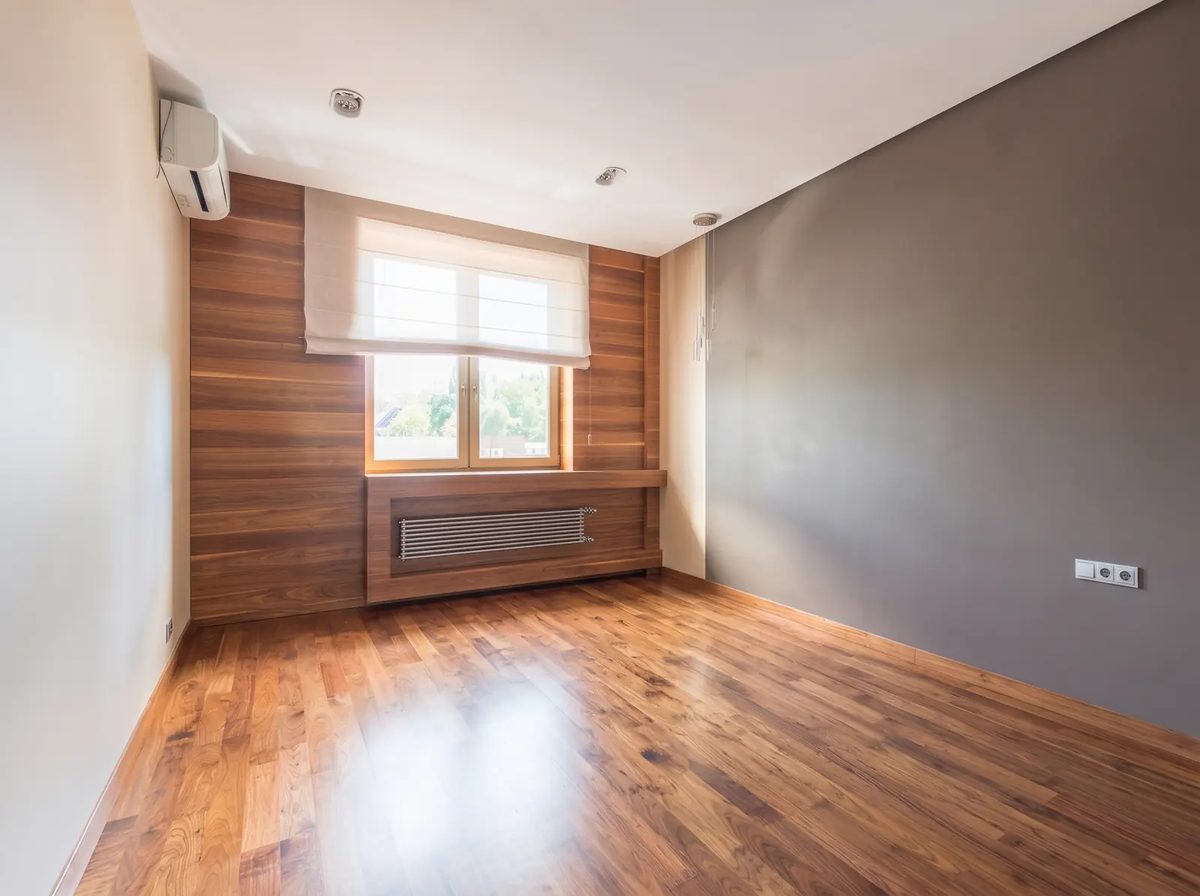 The same bedroom cleared of its furniture in the image, with the window, radiator and air conditioner in place